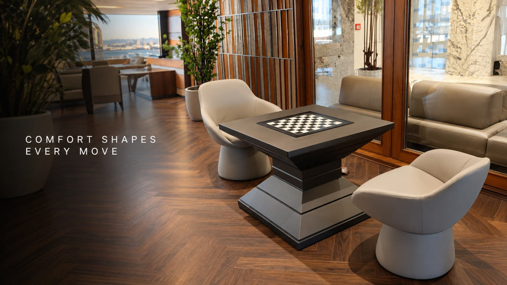 ARGMAC chess table with a black and white inlaid chess table top on a dark pedestal base, paired with two cream swivel chairs by a window.