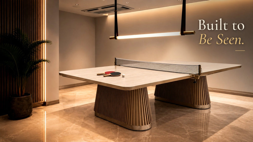 ARGMAC designer table tennis table with a light wood top and fluted pedestal bases, under a brass linear pendant light in a luxury game room with marble floors, with the text “Built to Be Seen.”